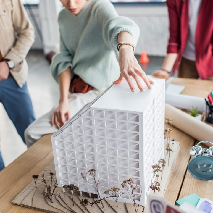 cropped view of group of female and male architects working together on house model in loft office